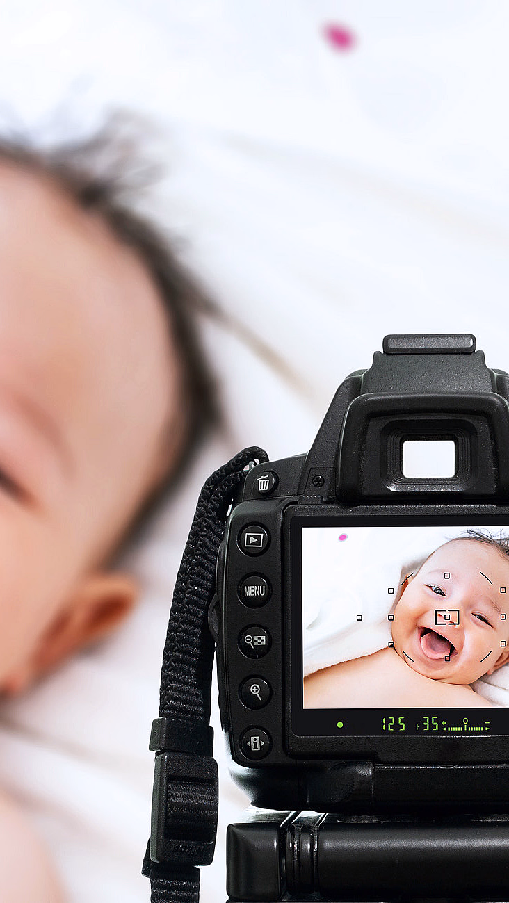 Hånd som holder et digitalkamera som viser en smilende baby på skjermen