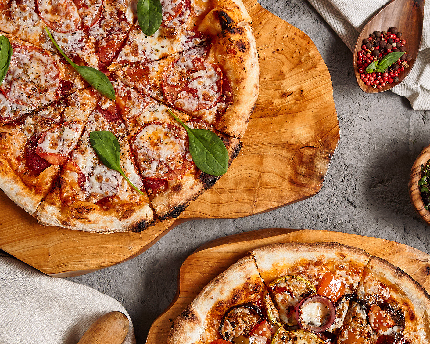 To pizzaer på trefjøler med tomat, spinat og aubergine ved siden av en treskje med pepperkorn