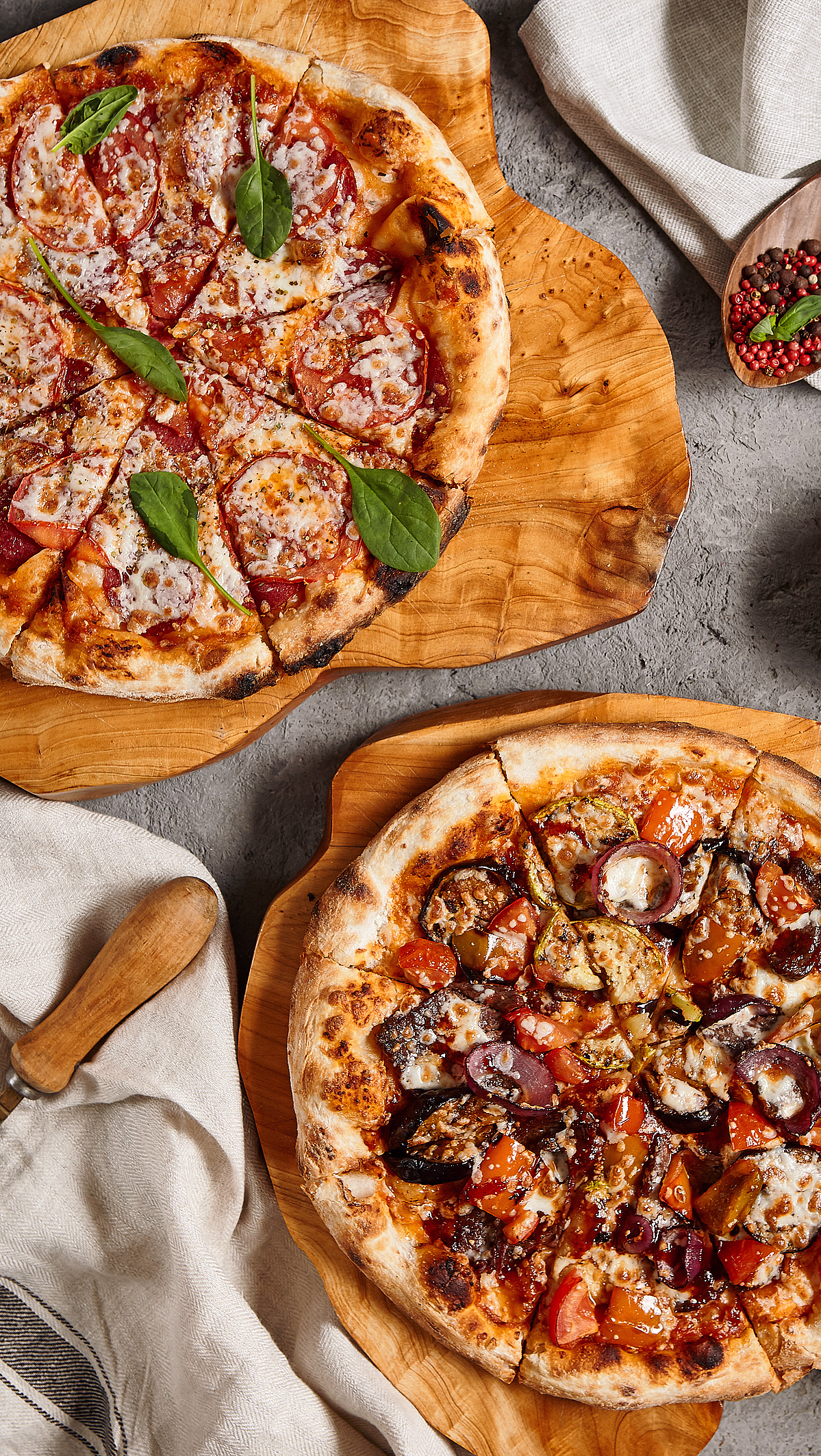 To pizzaer på trefjøler med tomat, spinat og aubergine ved siden av en treskje med pepperkorn