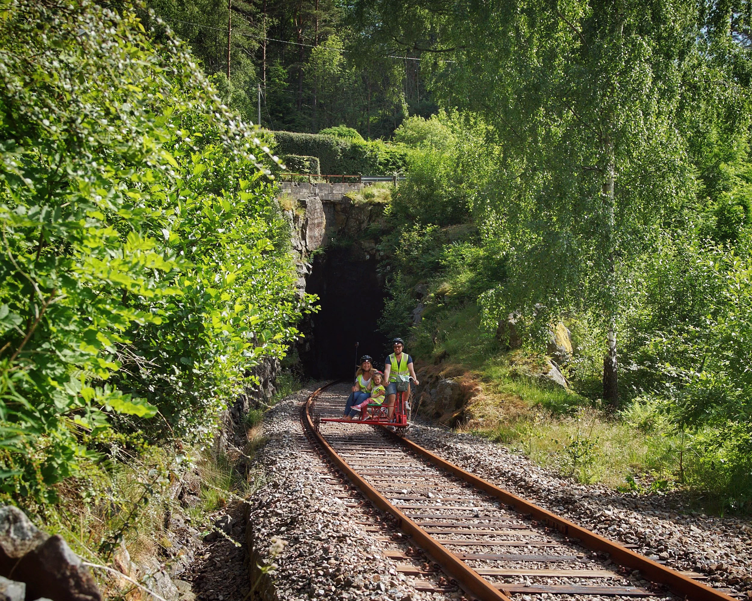 To personer på dresin på en jernbanelinje gjennom skog mot en tunnel