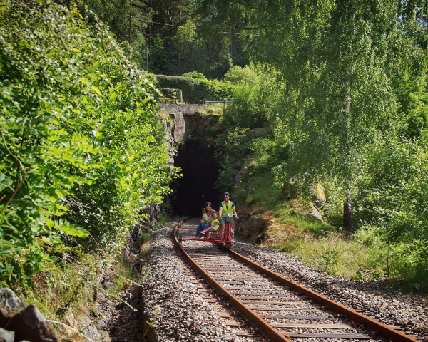To personer på dresin på en jernbanelinje gjennom skog mot en tunnel