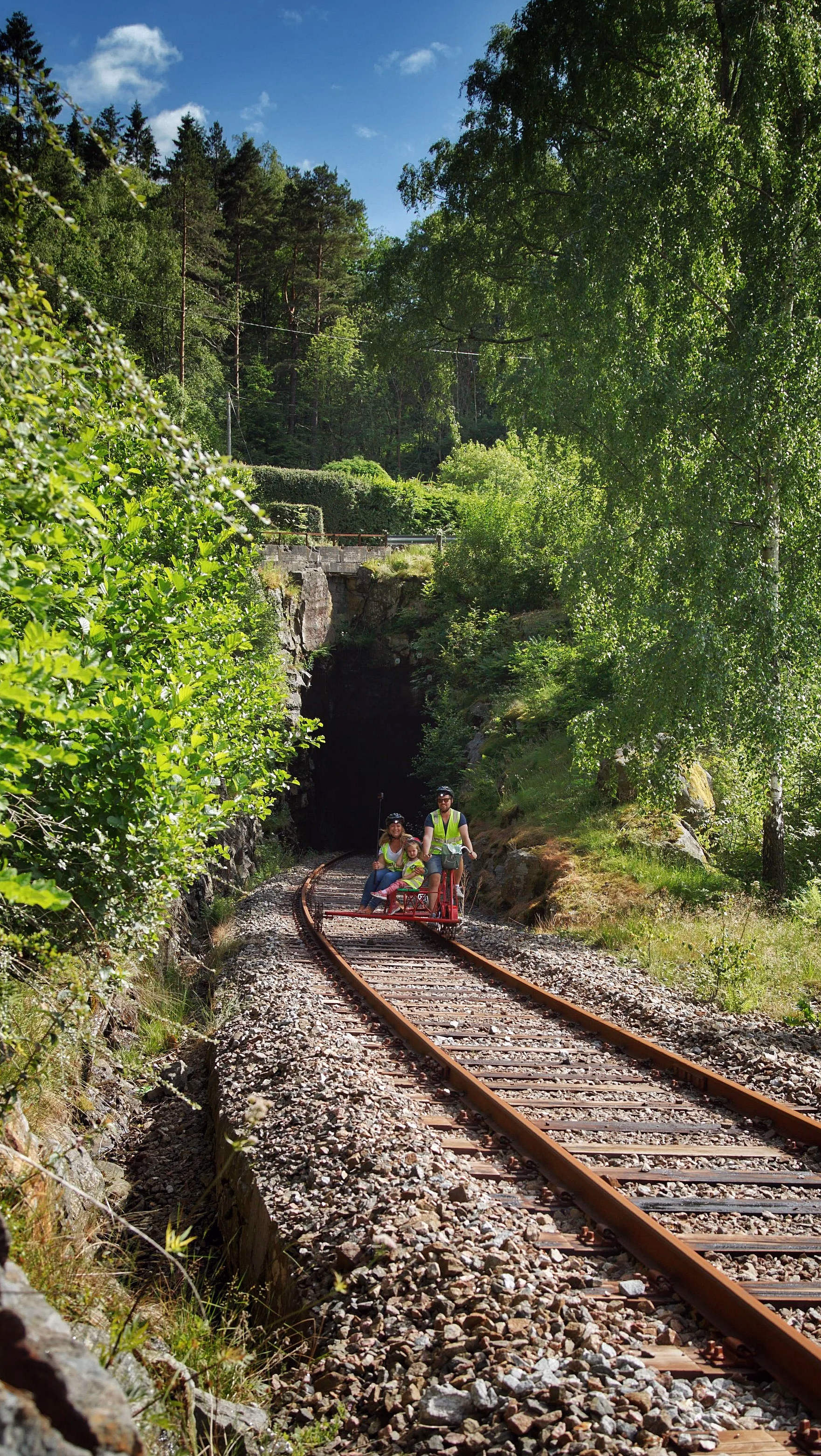 To personer på skinnesykkel gjennom grønn skog mot en tunnel