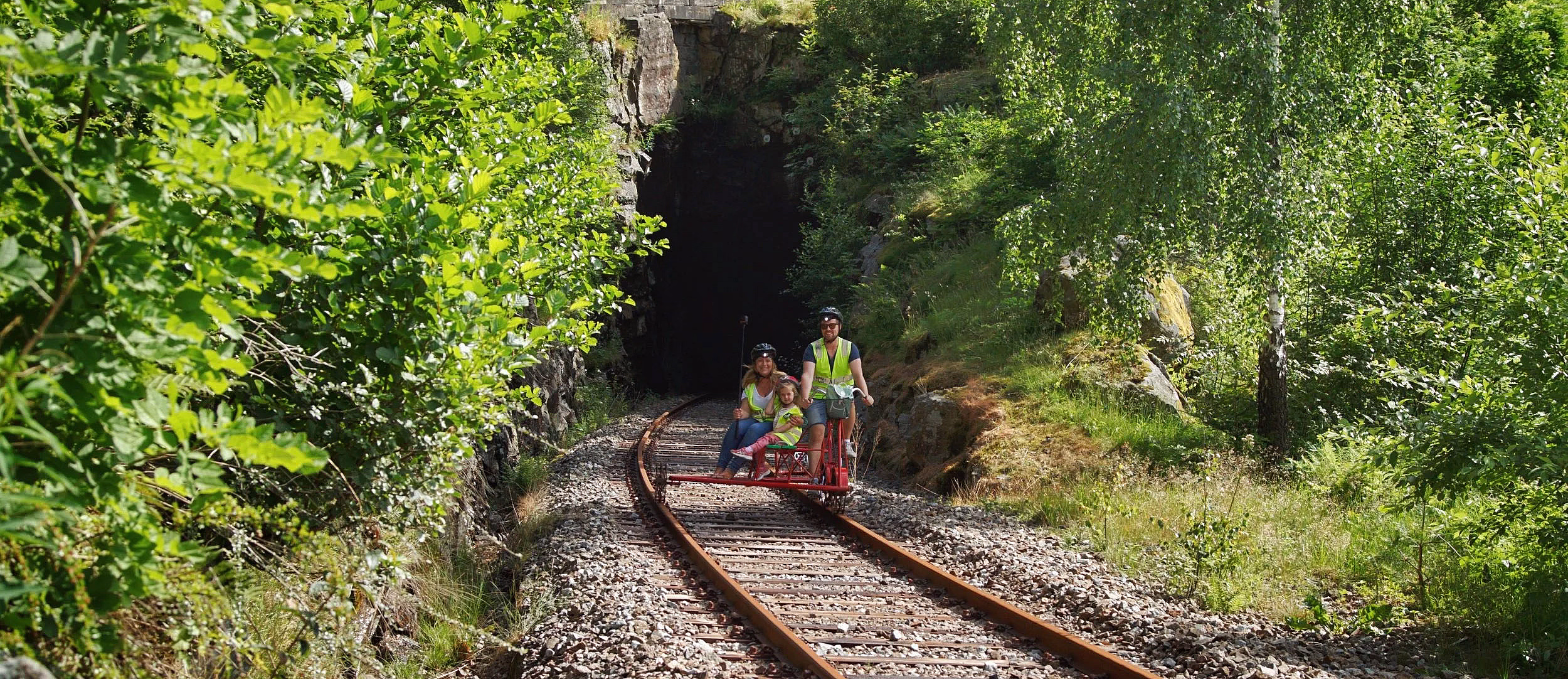 To personer på skinnesykkel gjennom grønn skog mot en tunnel
