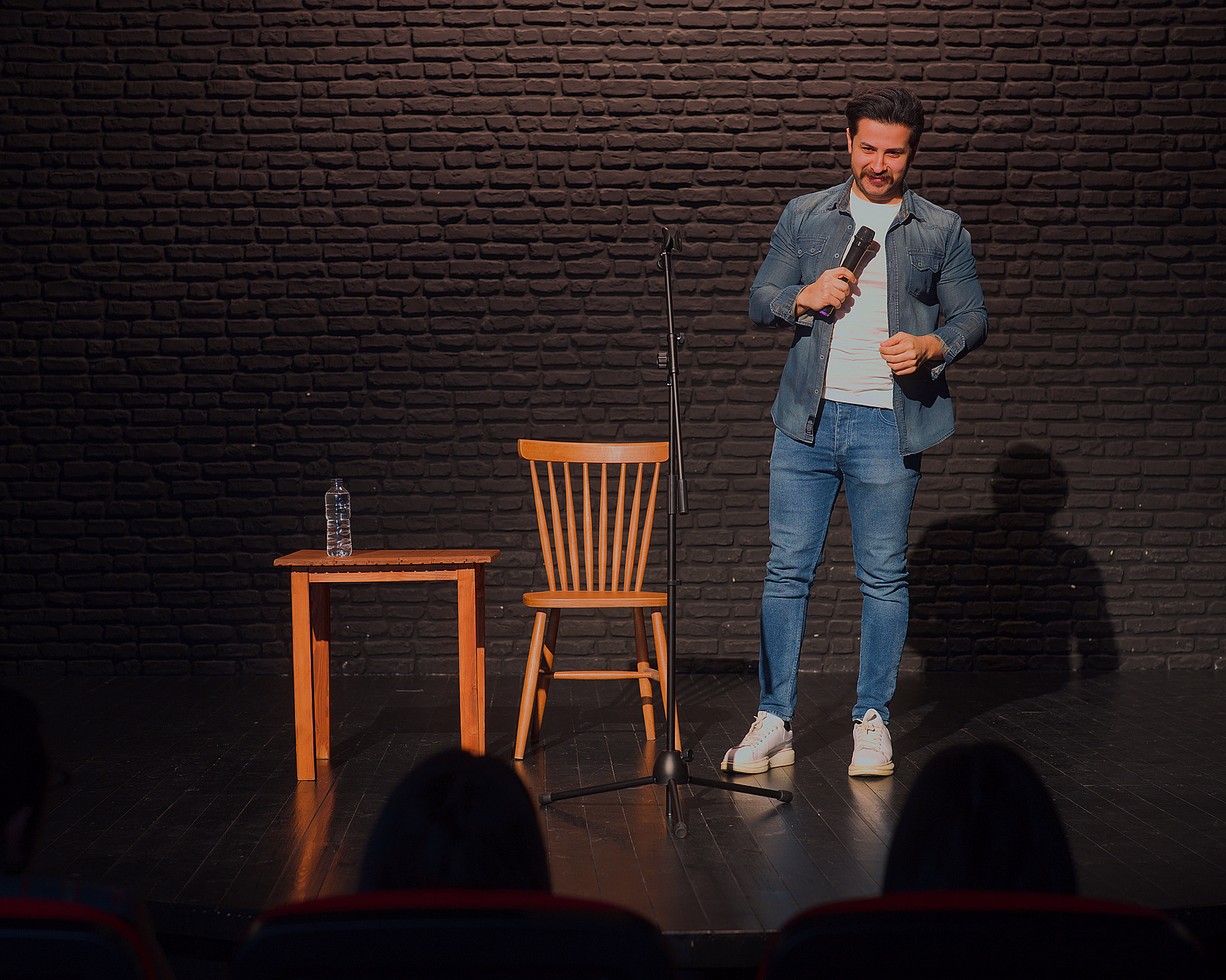 Mann med mikrofon på en scene foran en mørk murvegg og et publikum