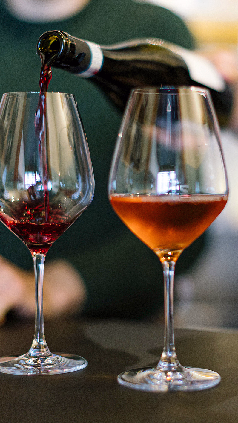 Rødvin helles i et glass ved siden av tre andre glass med ulik vin