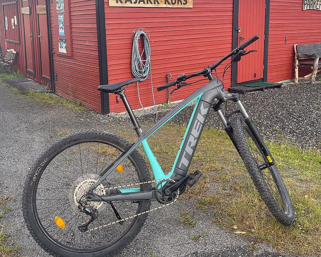 En rød trebygning med en kajakk på taket, en sykkel parkert foran og et skilt med teksten «KAJAKK KURS».