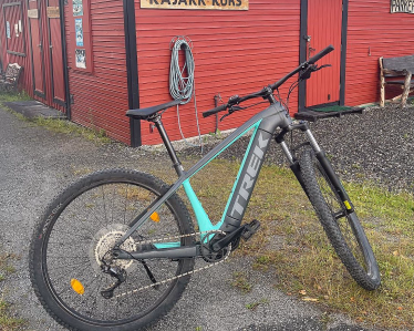 En rød trebygning med en kajakk på taket, en sykkel parkert foran og et skilt med teksten «KAJAKK KURS».