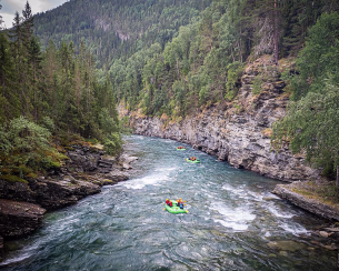 Rafting i grønne gummibåter på en elv som renner mellom bratte klipper og tett skog.