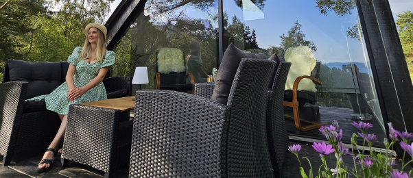 Kvinne i grønn kjole sitter på en terrasse foran en moderne hytte med store glassflater