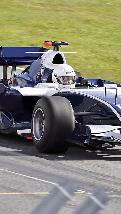 Blå og hvit formel 1-bil med nummer 16 i fart på en racerbane.
