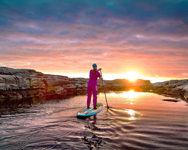 Person på et padlebrett i vannet ved solnedgang