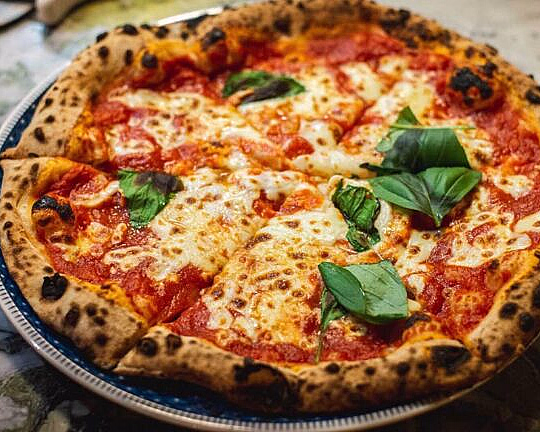 Nystekt pizza med sprø, brent skorpe, mozzarella, tomatsaus og fersk basilikum på en tallerken med blå kant og marmorbakgrunn.