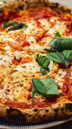 Nystekt pizza med sprø, brent skorpe, mozzarella, tomatsaus og fersk basilikum på en tallerken med blå kant og marmorbakgrunn.
