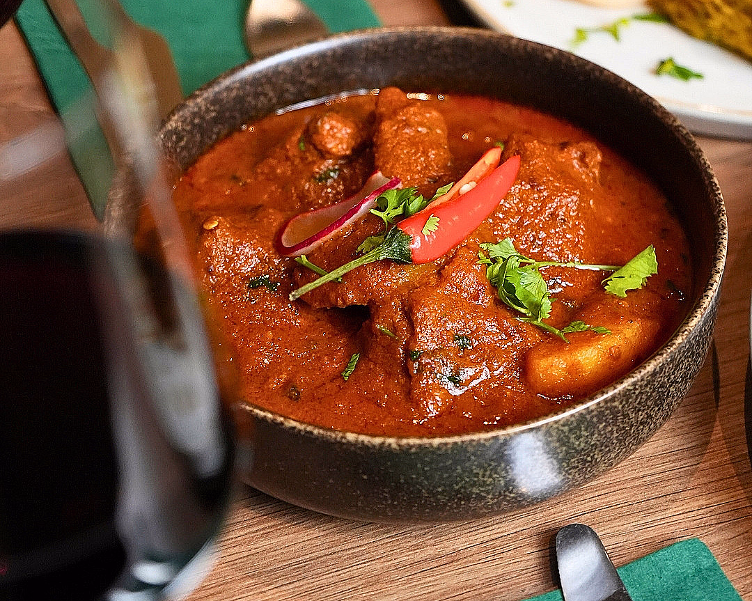 En mørk bolle med rød curry og kjøtt, toppet med chili og koriander, servert på et trebord med en grønn serviett.