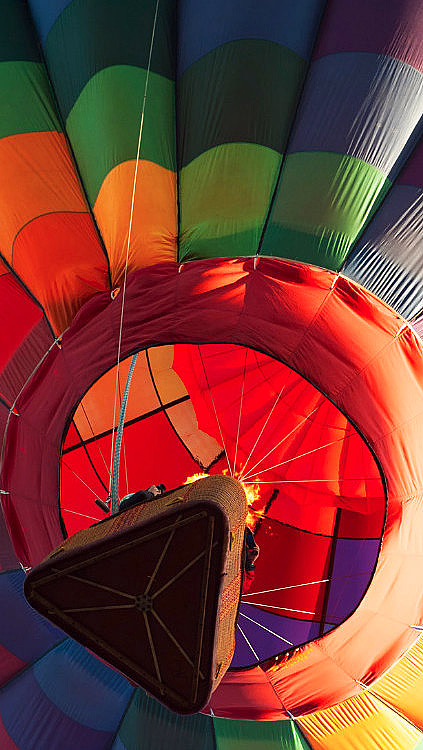 Fargerik luftballong med regnbuestriper sett nedenfra mot en klar blå himmel.