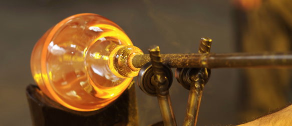 Glødende glass som formes på en metallstang i et glassblåserverksted