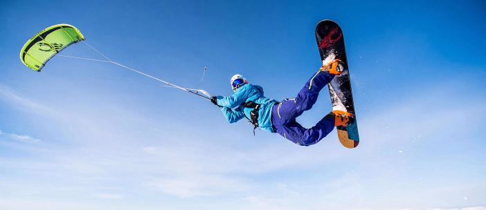 Person på snowboard som hopper med en kite over et snødekt landskap