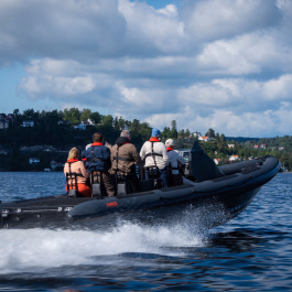 Gruppe med folk i en sort RIB-båt som kjører fort på vannet