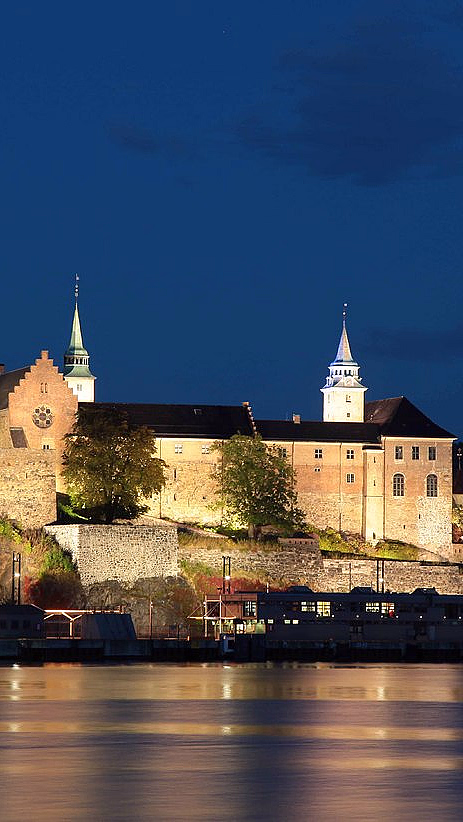 Opplyst festning ved vannet i kveldsmørket
