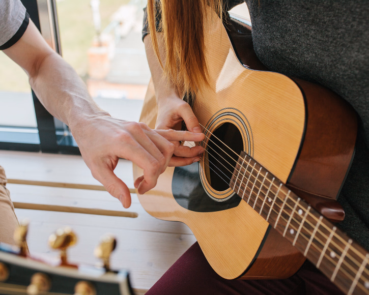 Nærbilde av en person som får veiledning i å plassere fingrene på strengene til en akustisk gitar
