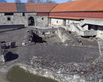 Historiske trebygninger og en moderne glasskonstruksjon rundt en ruin på Hedmarksmuseet