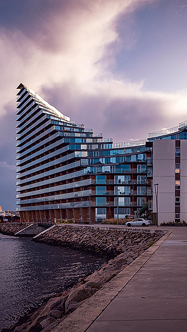 Moderne leilighetsbygg ved vannet med en bølgeformet fasade under en overskyet himmel