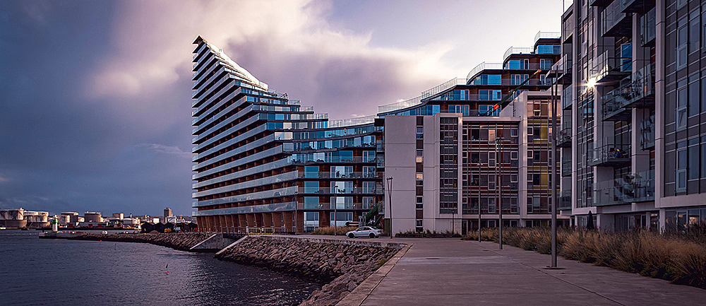 Moderne leilighetsbygg ved vannet med en bølgeformet fasade under en overskyet himmel
