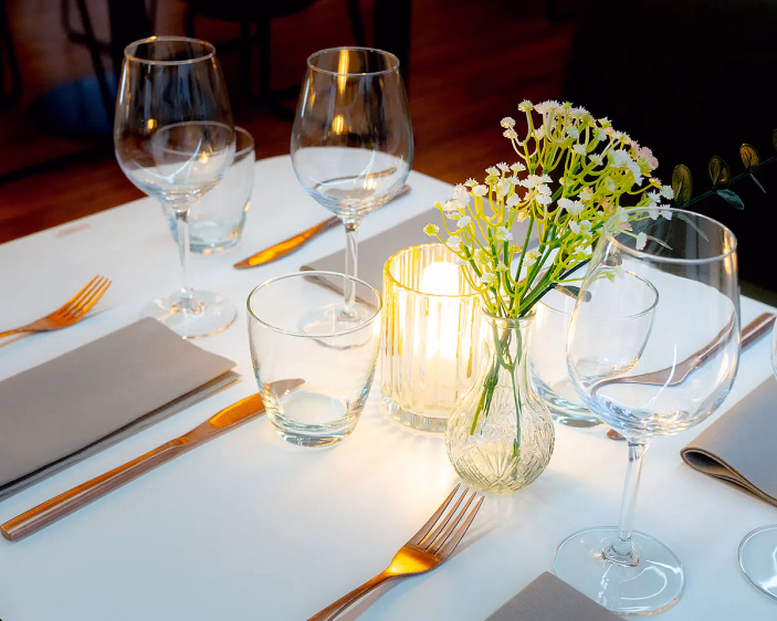 Dekket bord med vinglass, bestikk, telys og en liten blomstervase