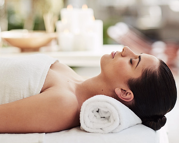 En kvinne som slapper av på spa, pakket inn i et hvitt håndkle med lukkede øyne og stearinlys i bakgrunnen.