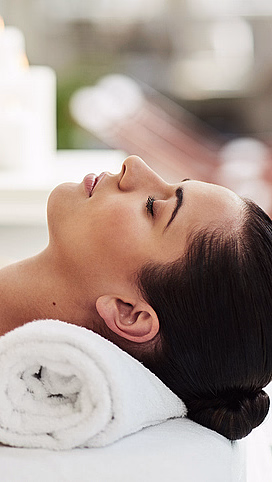 En kvinne som slapper av på spa, pakket inn i et hvitt håndkle med lukkede øyne og stearinlys i bakgrunnen.