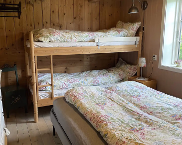 Soverom med trevegger, køyeseng og en dobbeltseng med blomstrete sengetøy