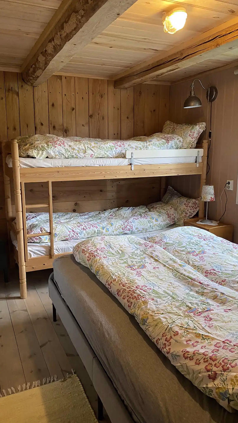 Soverom med trevegger, køyeseng og en dobbeltseng med blomstrete sengetøy