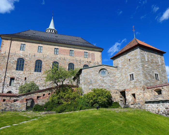 Gammel festning i stein med tårn og grønn plen under en blå himmel