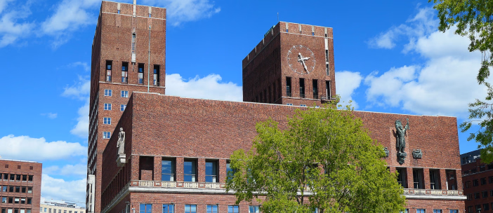 Oslo rådhus i murstein med to tårn og en stor klokke under en blå himmel