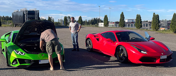 En lysegrønn Lamborghini med åpent bagasjerom foran og en rød Ferrari parkert på en asfaltert plass under en blå himmel.