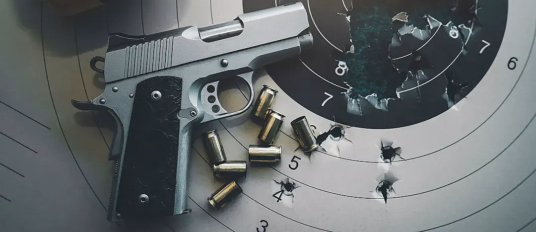 Sølvfarget pistol med svart grep på en papirblink med kulehull, tomhylser i messing og gule hørselvern.