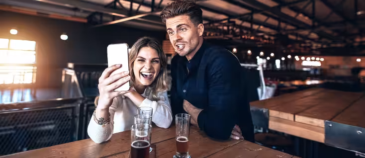 Mann og kvinne tar en selfie ved et bord med ølglass i et lokale med industritak