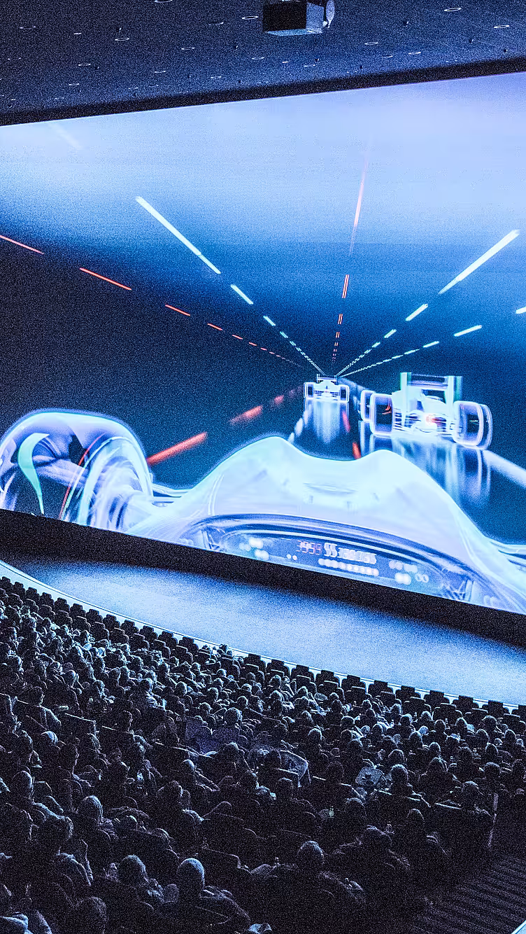 Publikum i en kinosal som ser på en stor skjerm med racerbilmotiv og IMAX-logo på veggen