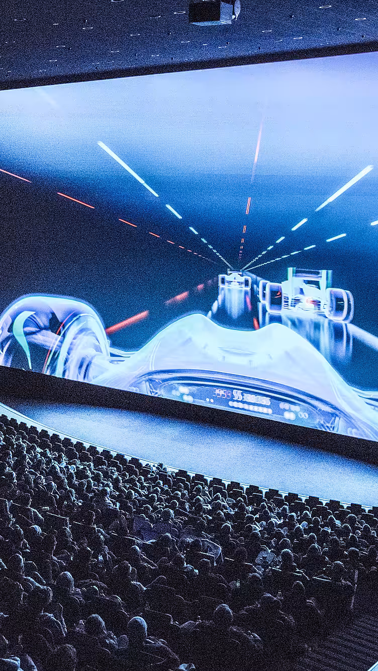 Publikum i en kinosal som ser på en stor skjerm med racerbilmotiv og IMAX-logo på veggen