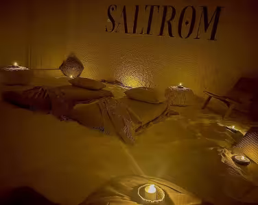 Madrasser og tepper på et sandgulv i et dempet belyst rom med teksten SALTROM på veggen