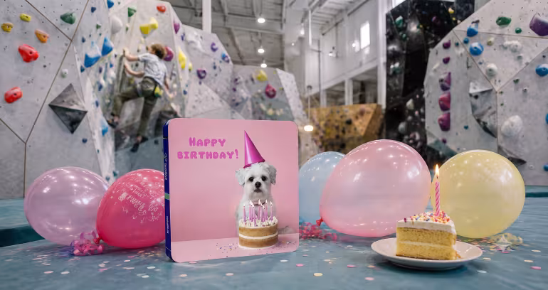 Gavekort med hund og teksten Happy Birthday foran klatrevegg med kake og ballonger