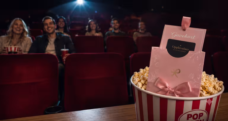 Et rosa gavekort i et beger med popcorn foran publikum i en kinosal