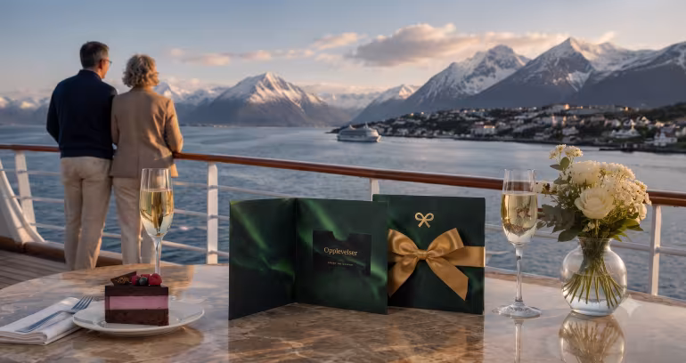 Par på et cruiseskip som ser ut over snødekte fjell, med et gavekort og kake på bordet