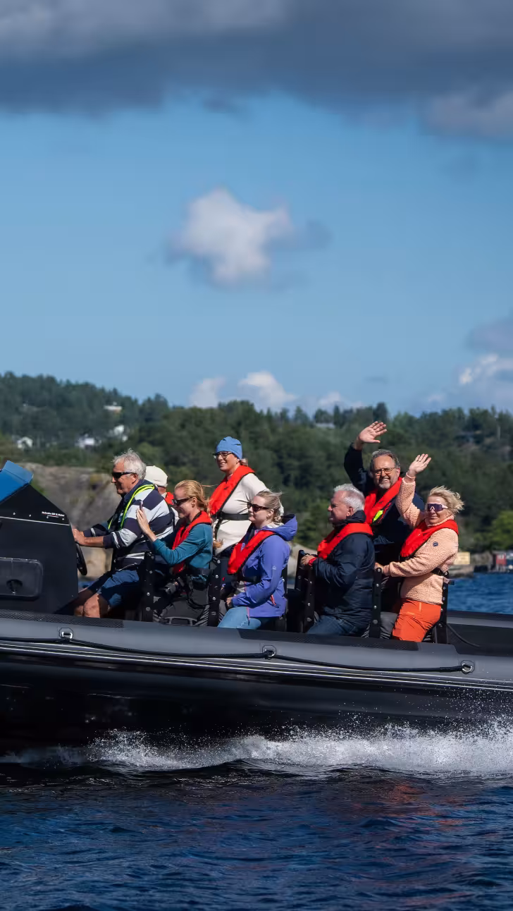 En gruppe mennesker i en RIB-båt på vannet langs en skogkledd kyst
