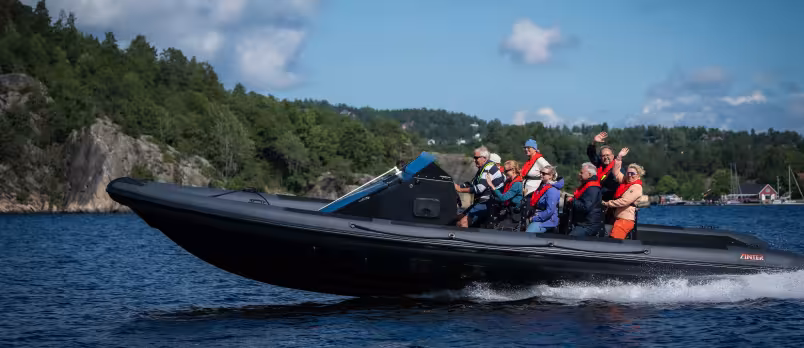 En gruppe mennesker i en RIB-båt på vannet langs en skogkledd kyst