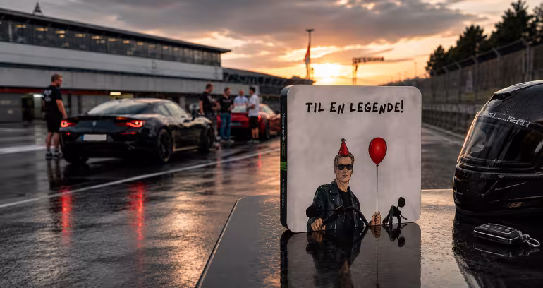 Gaveeske med teksten Til En Legende foran en racerbil og hjelm på en våt bane i solnedgang