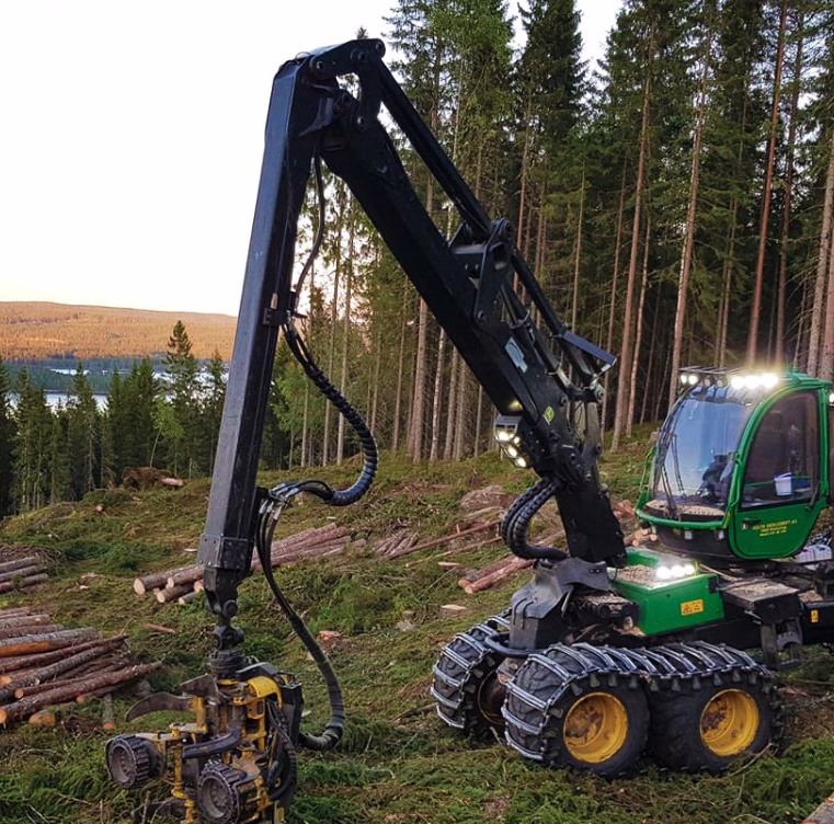 Grønn skogsmaskin på en åsside med tømmerstokker og en innsjø i bakgrunnen