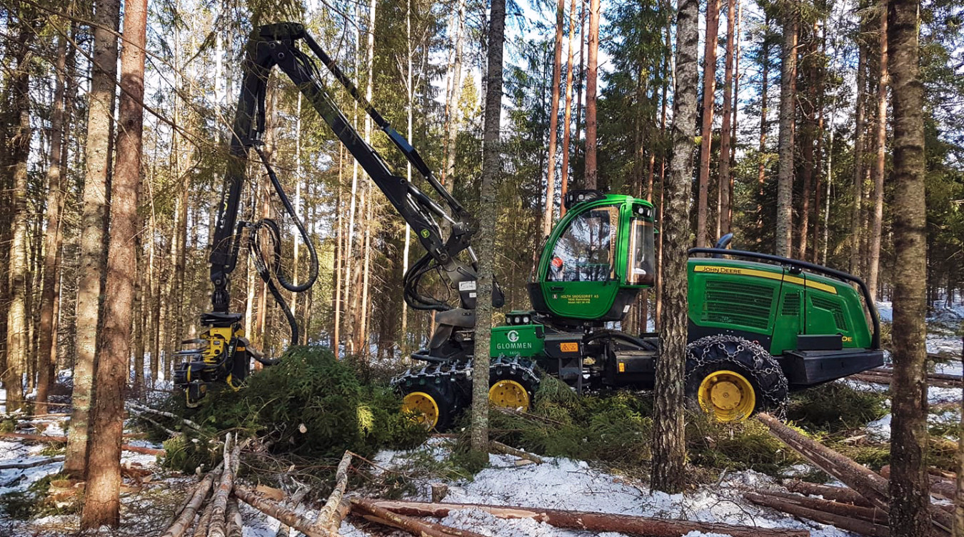 Grønn John Deere skogsmaskin med kranarm i en snødekket skog