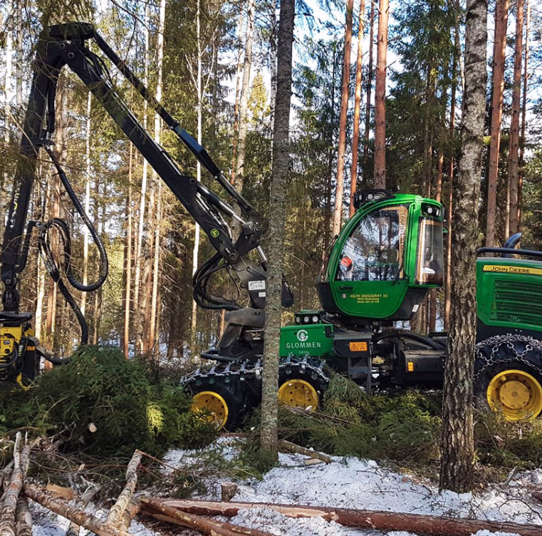 Grønn John Deere skogsmaskin med kranarm i en snødekket skog