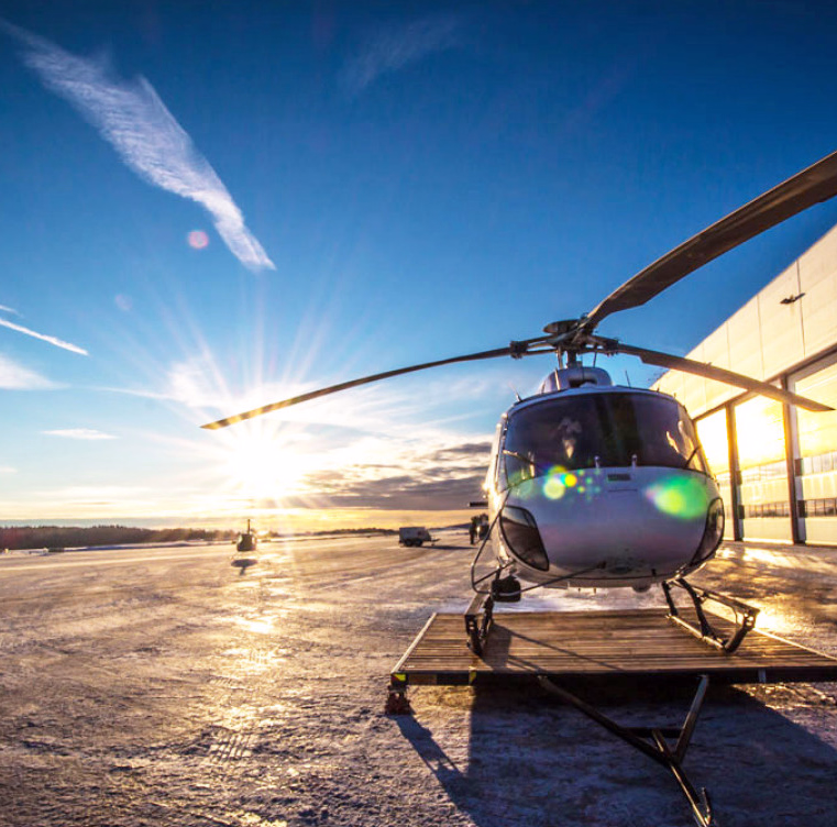 Sølvfarget helikopter på snødekket bakke ved en hvit bygning i lav sol